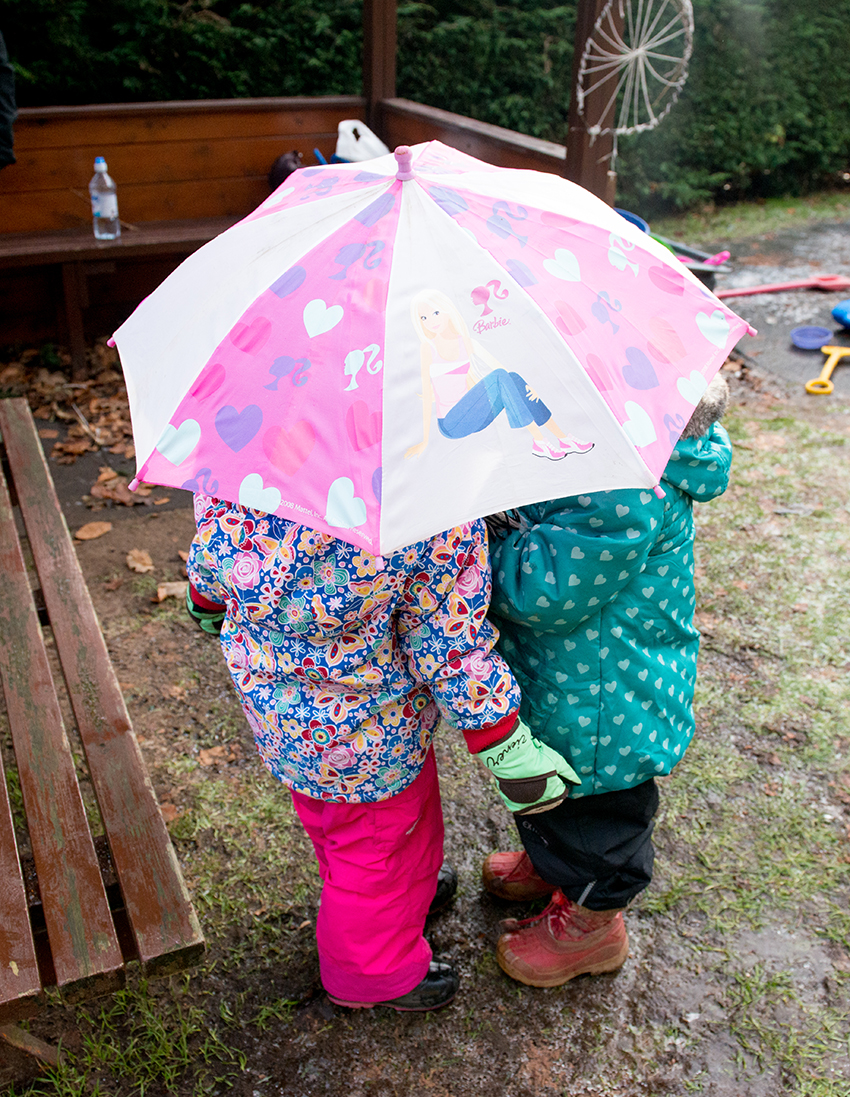 Photograph of children hiding under an umbrella