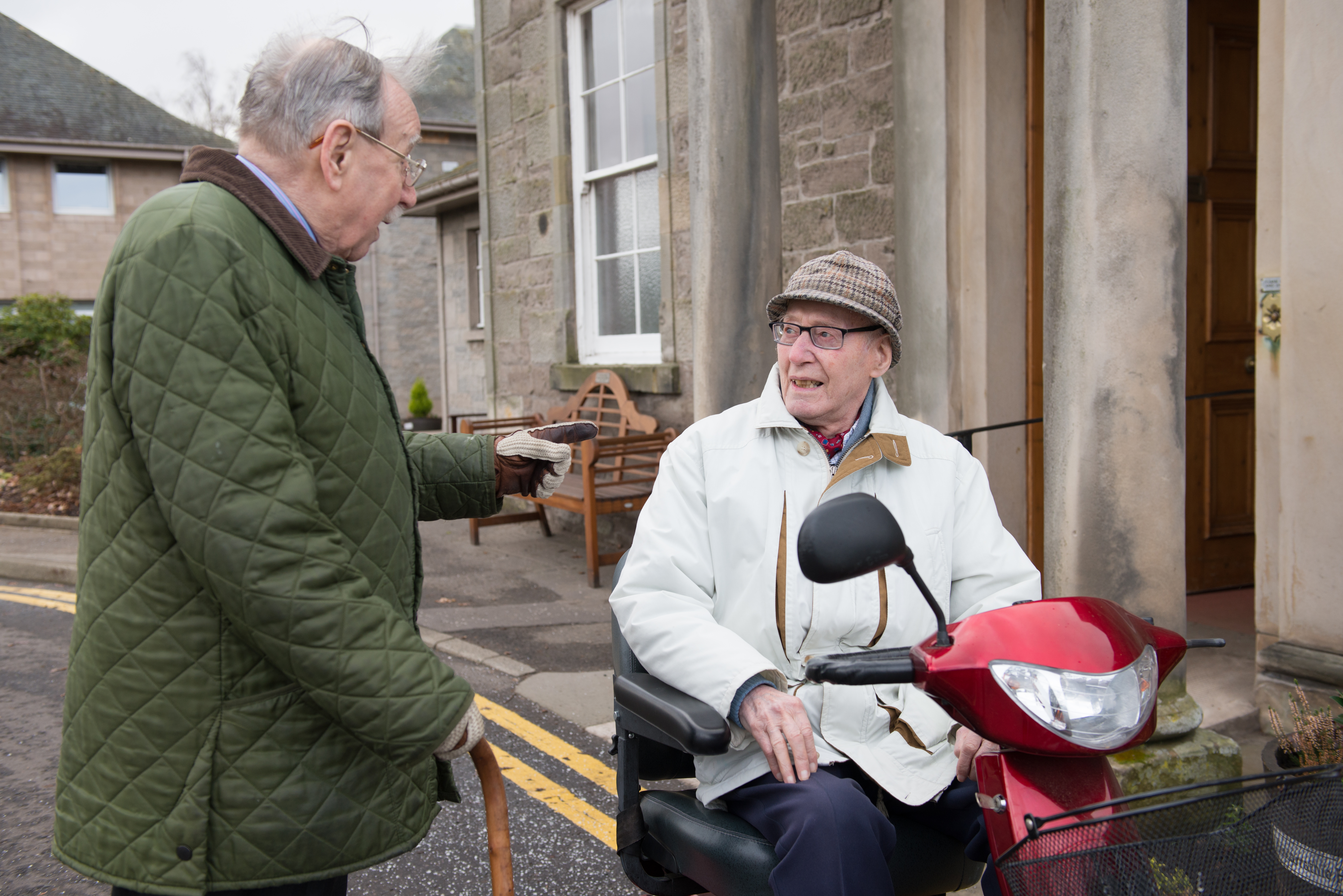 Two older men chatting outside. One is in a wheelchair and one is standing. 