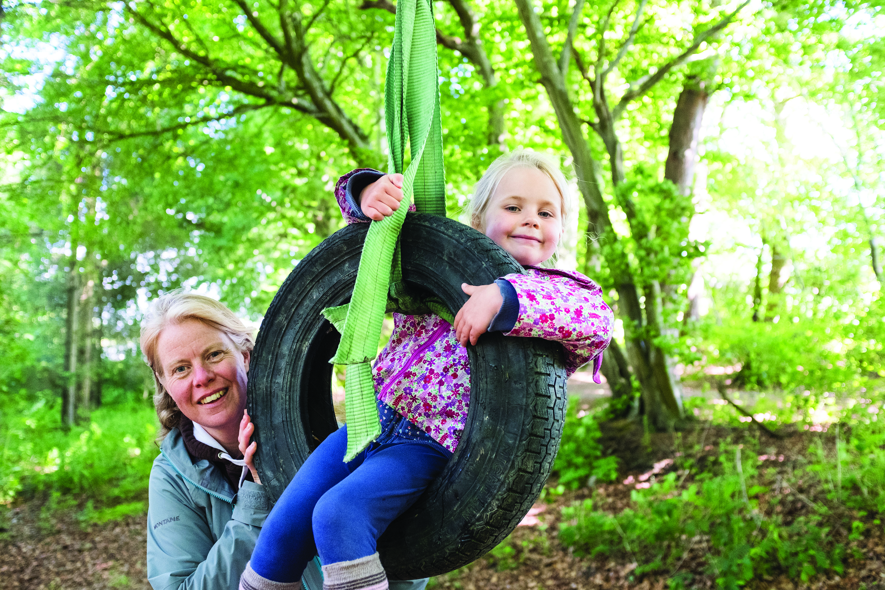 Childminder standing next to a child in a tyre swing