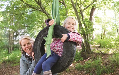 Childminder standing next to a child in a tyre swing