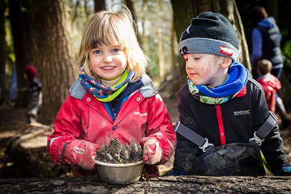 Two children playing outside collecting pinecones