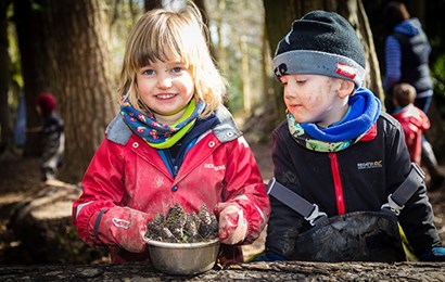 Two children playing outside collecting pinecones