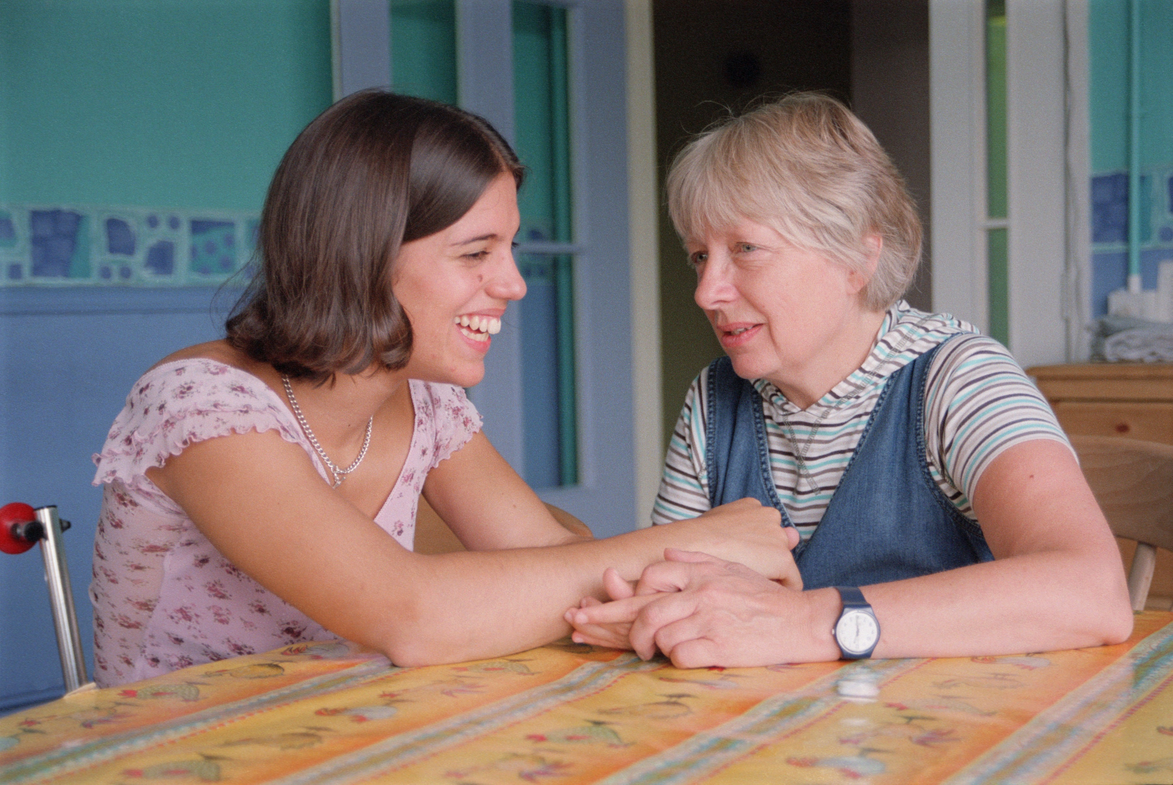 Younger and older ladies stitting at the table holding hands