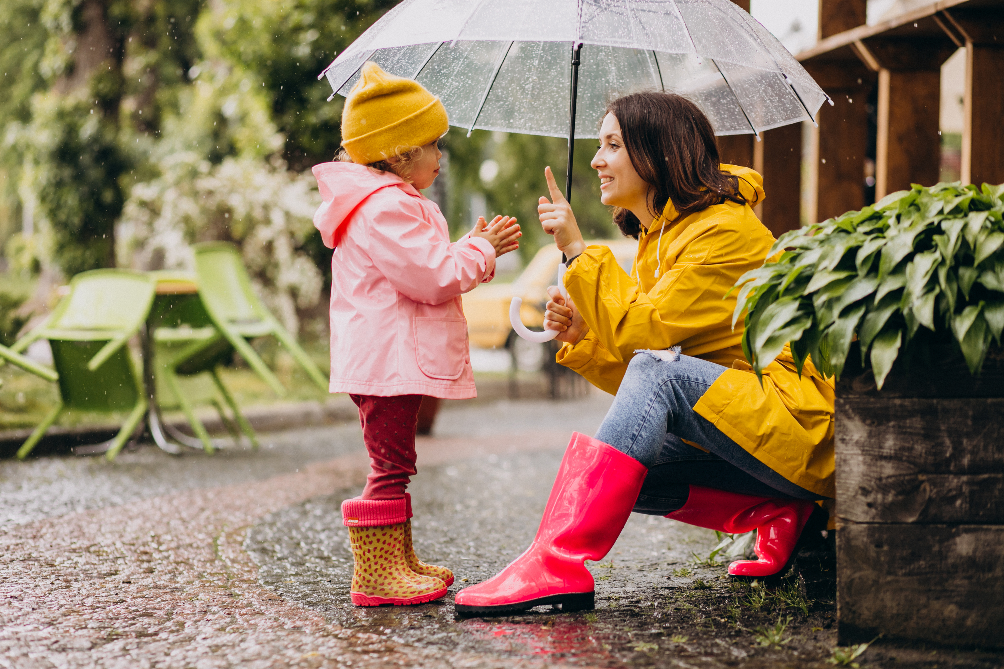 Mother with daughter standing under an umbrella wearing wellies and raincoats