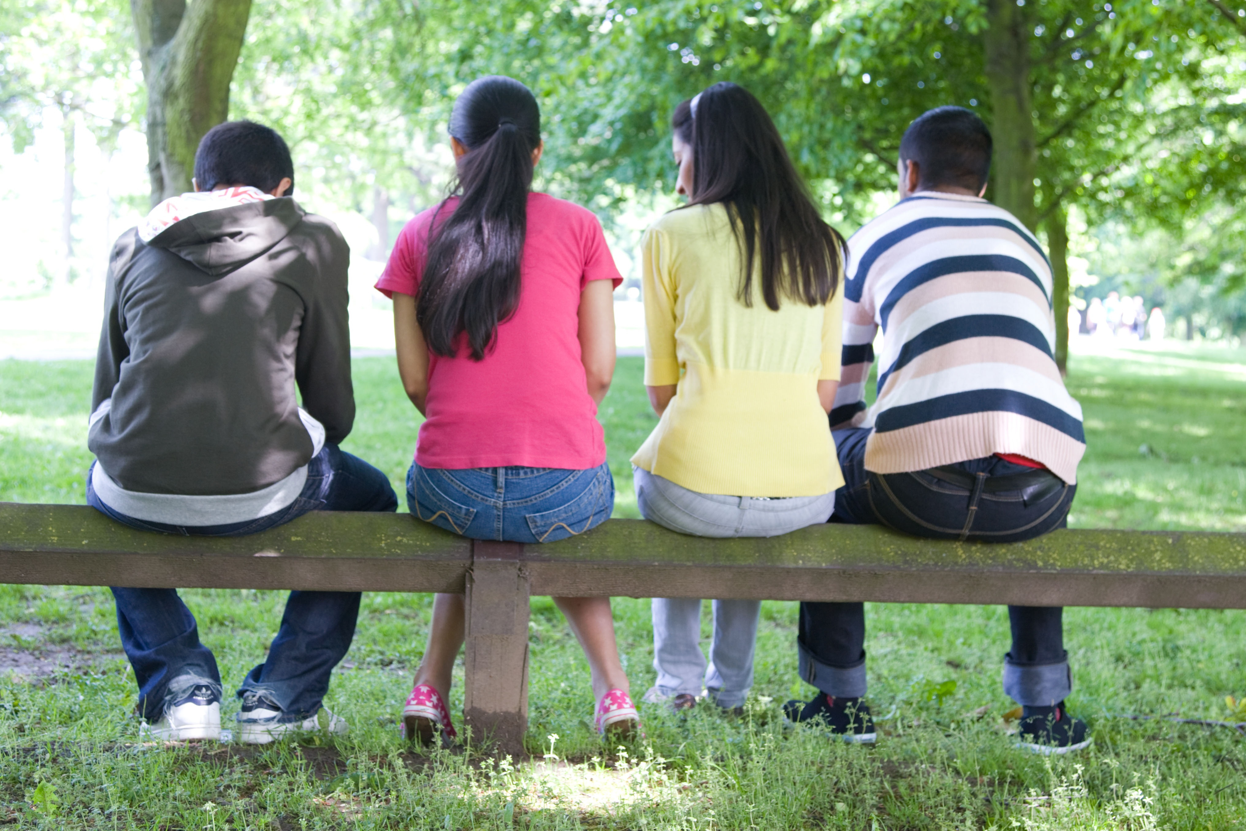 Group of young adults sitting on a bench facing away from the camera 