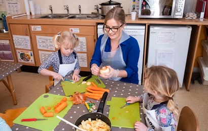 Staff and children cutting up vegetables in a nursery setting